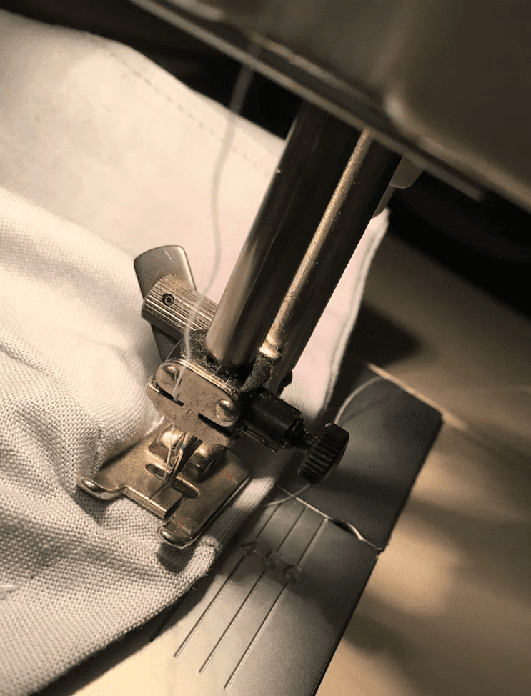 Close view of a sewing machine presser foot stitching pale fabric