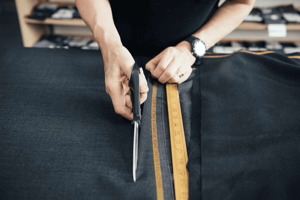 Shears cutting along a marked line on dark fabric, beside a tape measure