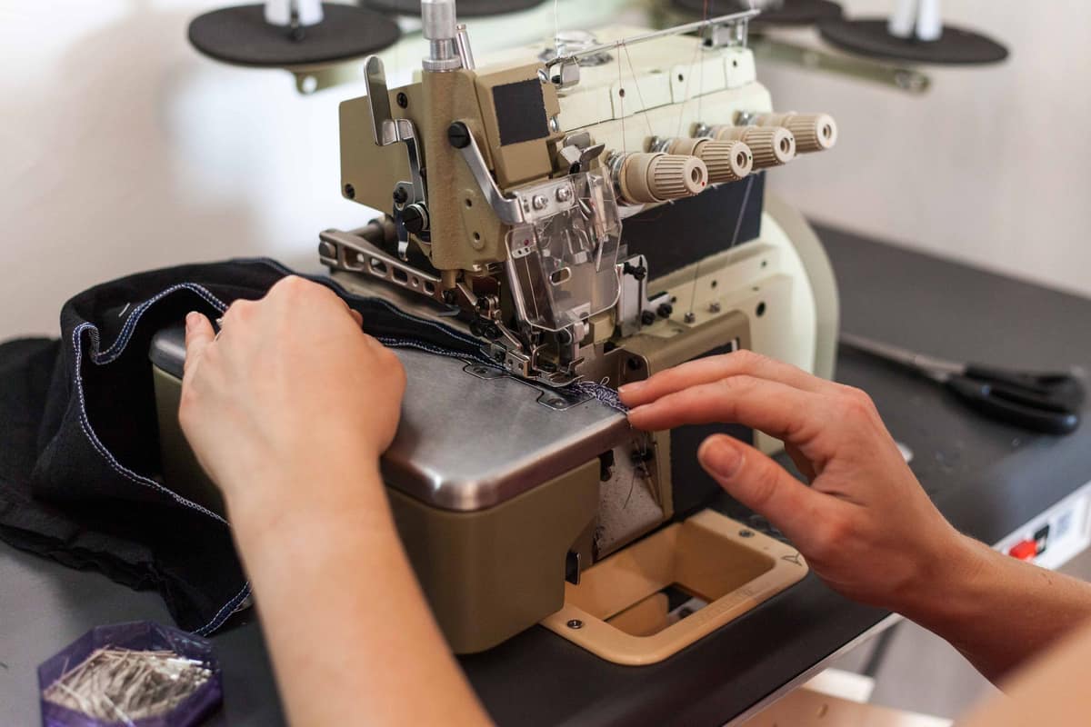 Hands guiding dark fabric through an industrial overlock, the finished seam edge visible