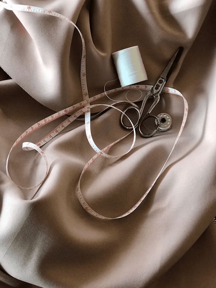 Blush satin with a tape measure, thread and tailoring shears laid across it